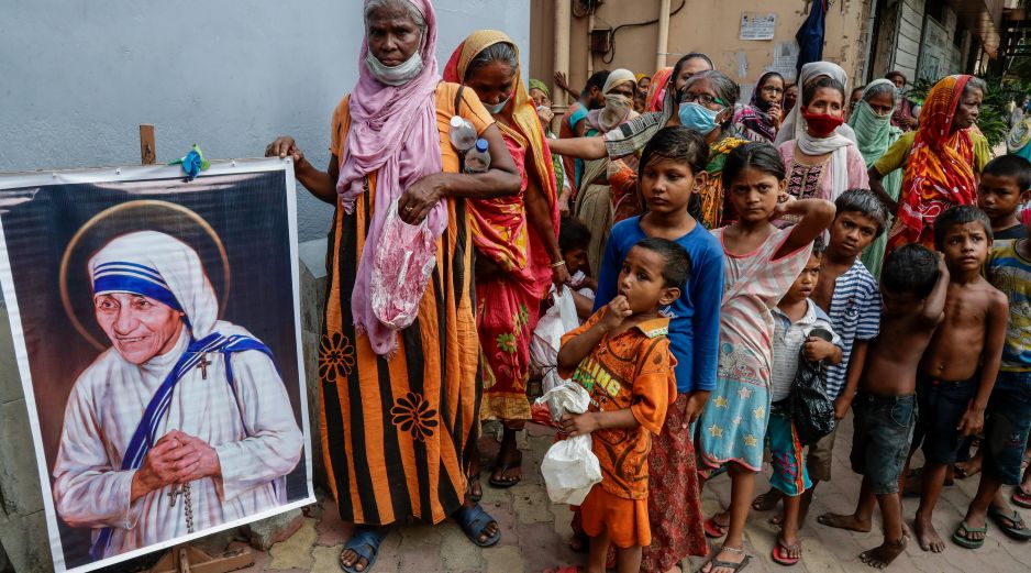 Personas sin hogar al lado de un cuadro de santa Teresa de Calculta afuera de la sede de las Misioneras de la caridad. AP/B. Das