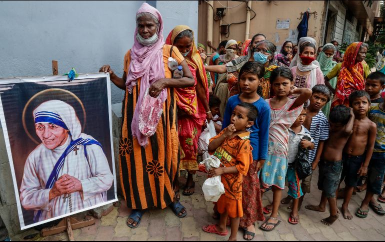 Personas sin hogar al lado de un cuadro de santa Teresa de Calculta afuera de la sede de las Misioneras de la caridad. AP/B. Das