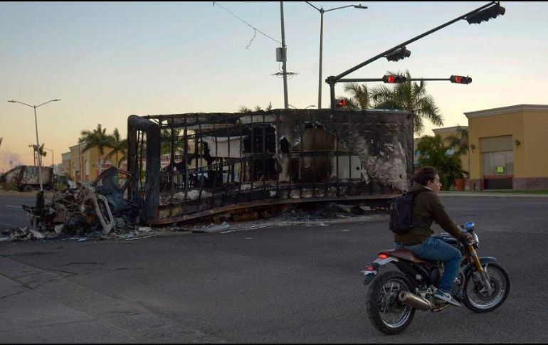 Un habitante de Culiacán camina cerca de los restos de un vehículo incendiado ayer jueves. AFP/J. Cruz